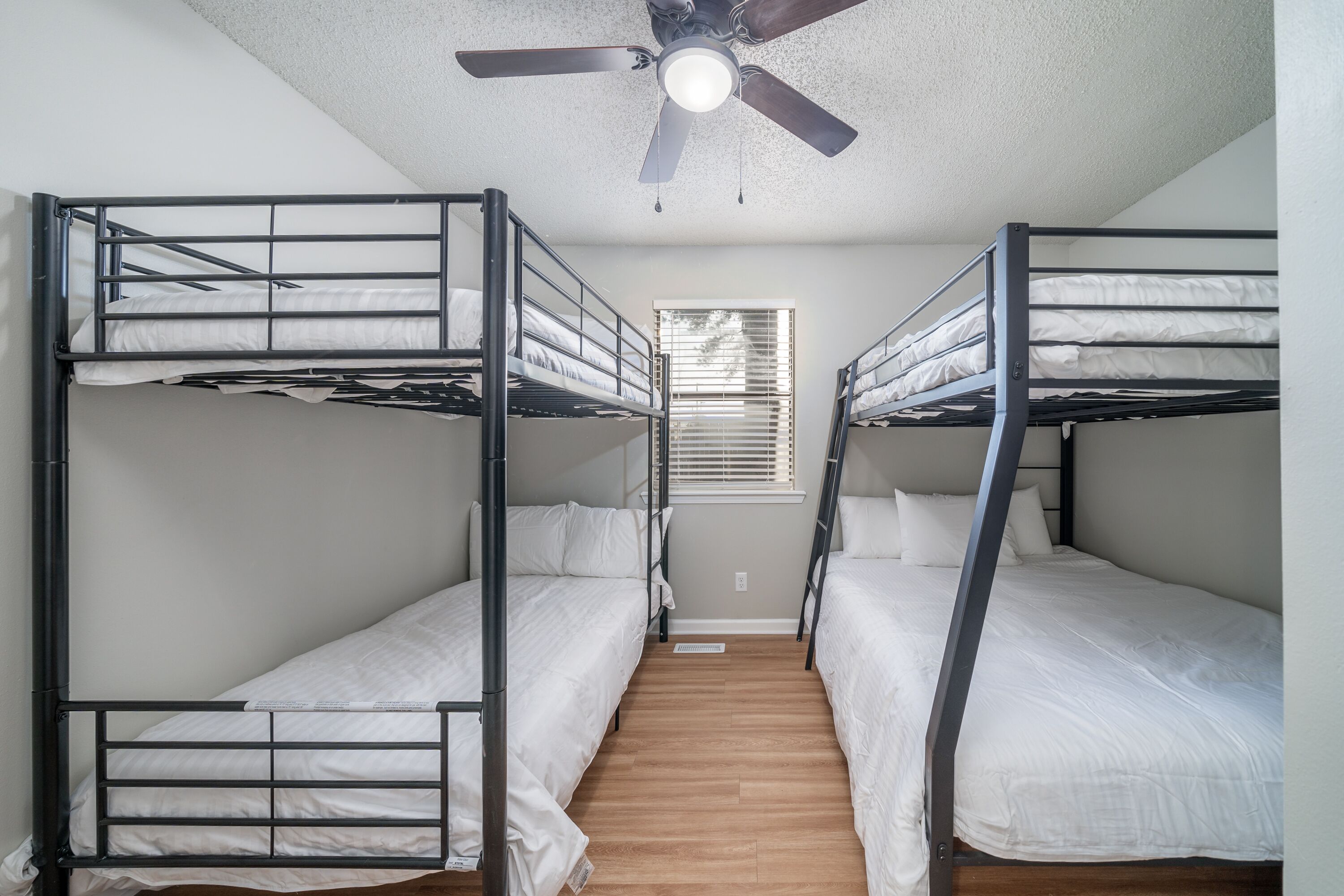 A room with bunk beds, a ceiling fan, and a window with blinds.