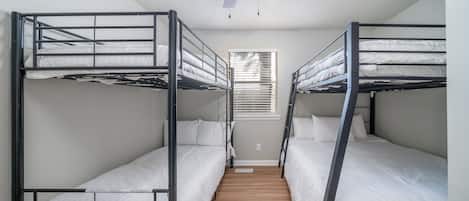 A room with bunk beds, a ceiling fan, and a window with blinds.