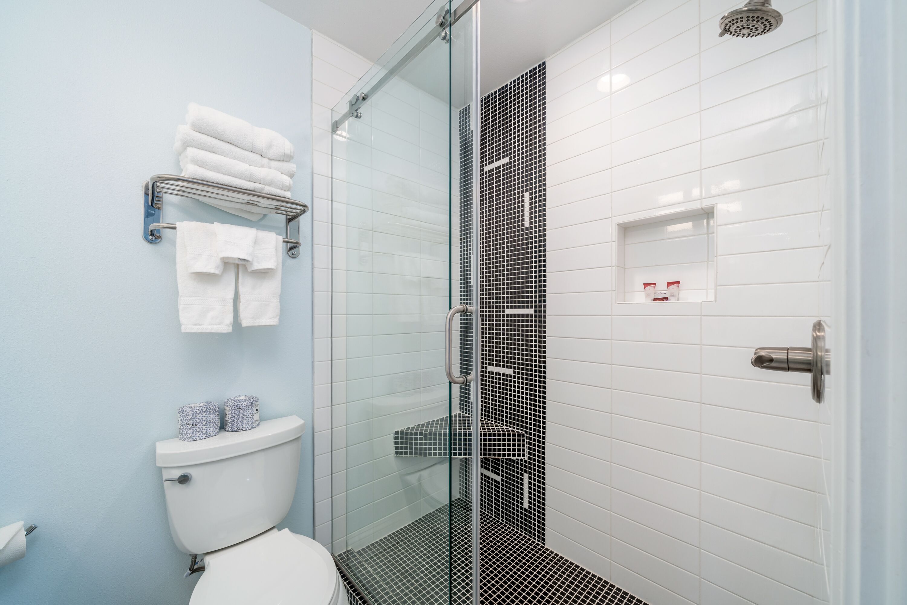 Une salle de bain moderne avec une douche à parois de verre, des murs recouverts de carreaux blancs et des toilettes dotées d’un meuble de rangement.