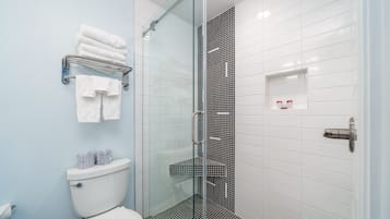 Une salle de bain moderne avec une douche à parois de verre, des murs recouverts de carreaux blancs et des toilettes dotées d’un meuble de rangement.