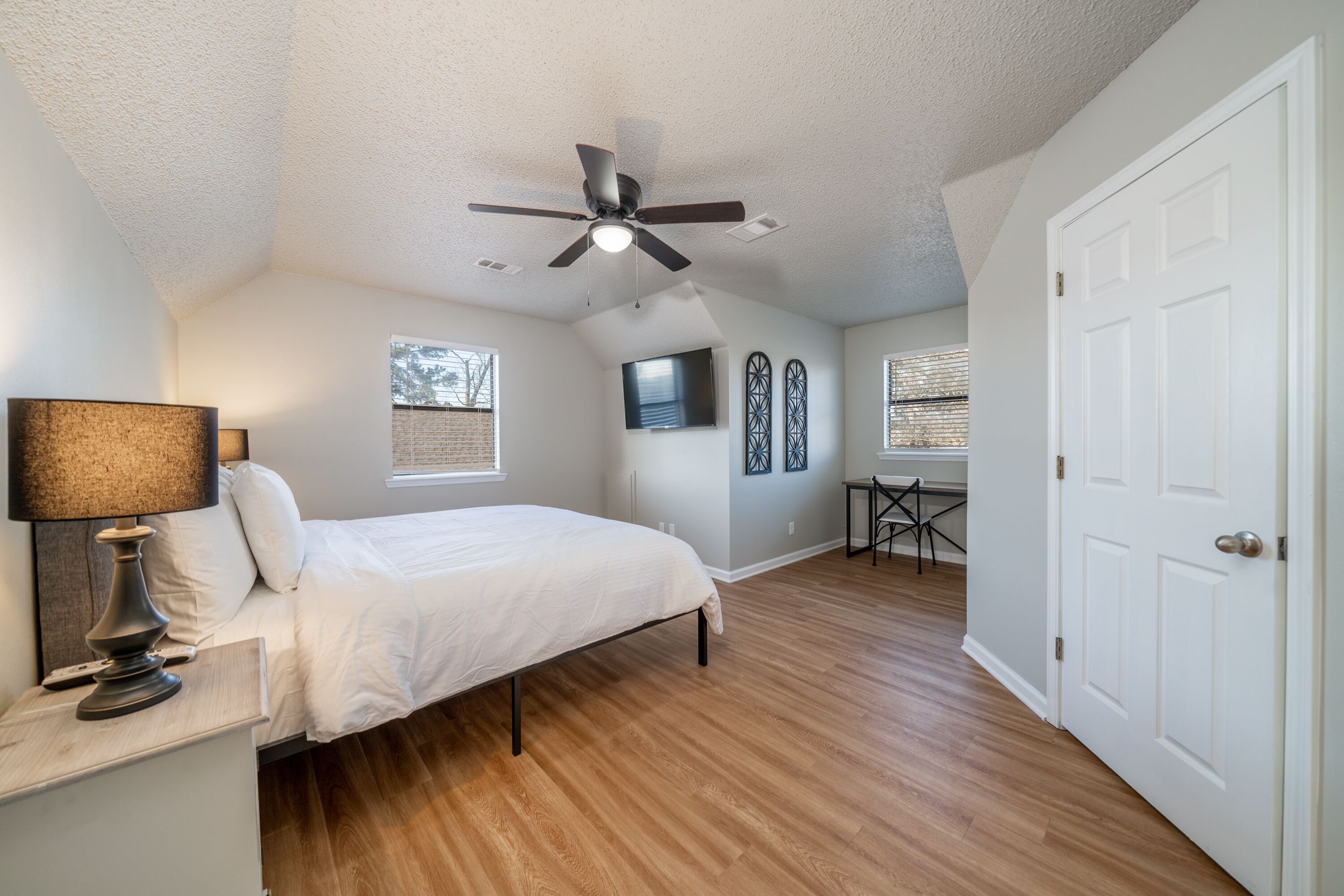 A bedroom with a bed, a ceiling fan, a TV, and a door.