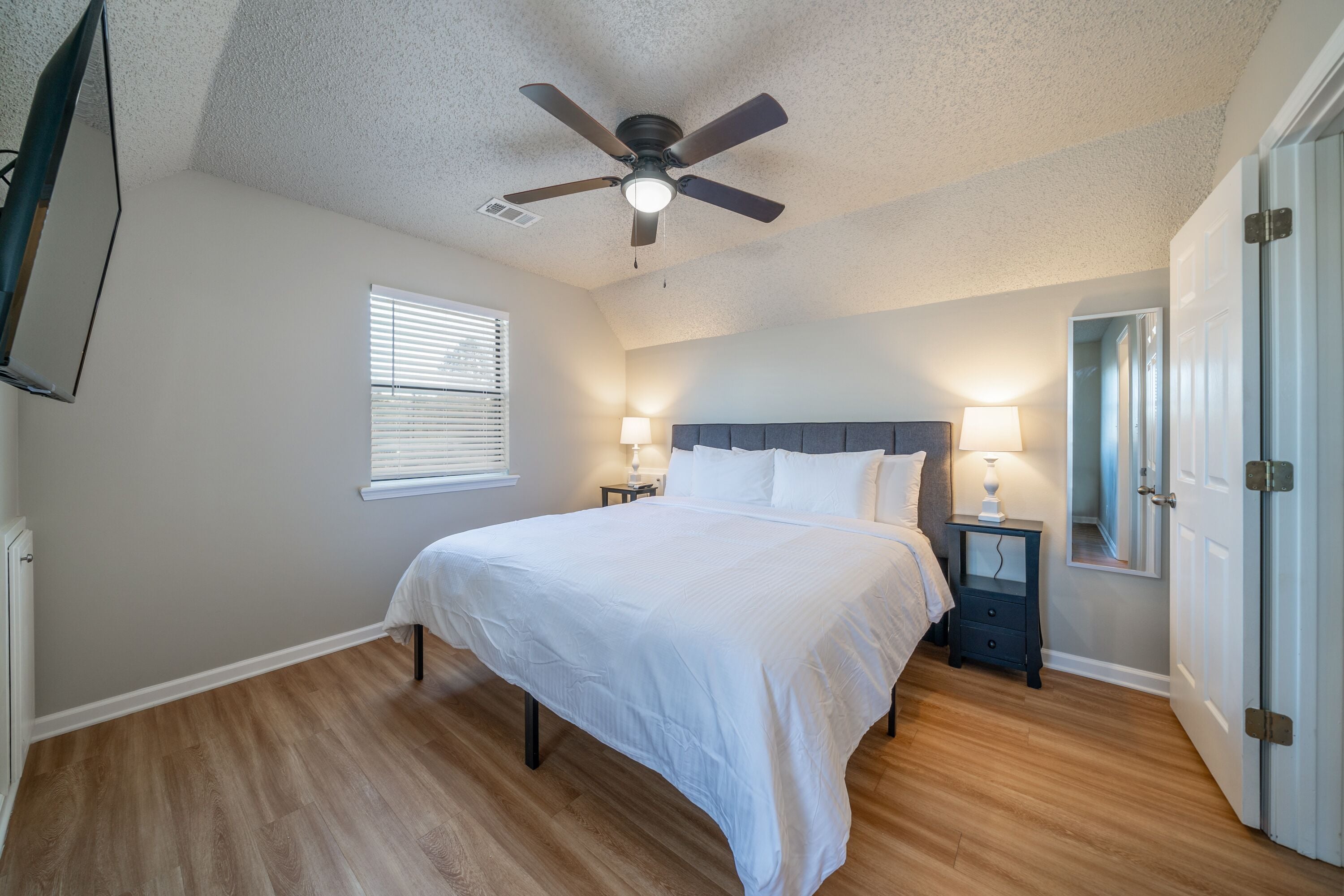 A bedroom with a bed, ceiling fan, bedside lamps, and a door.