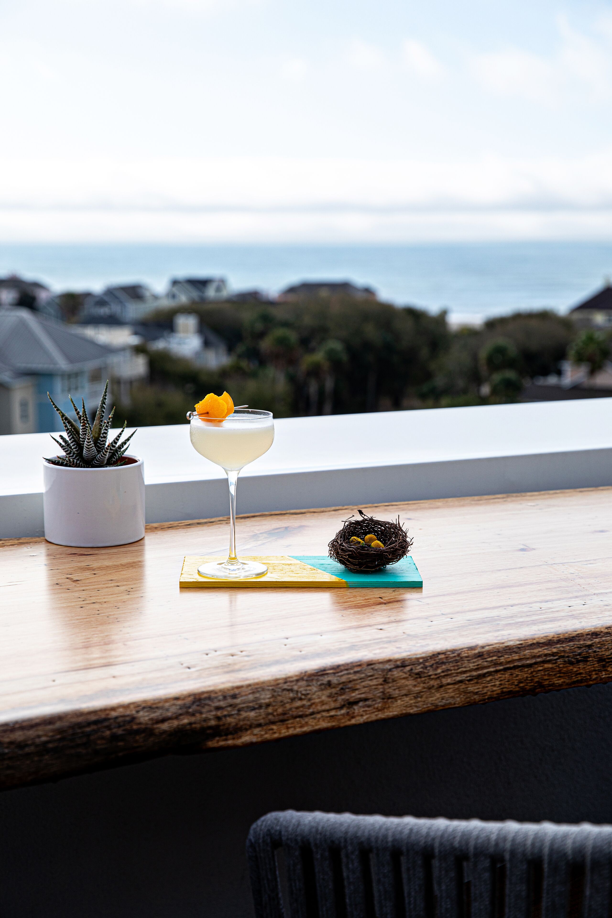 Een cocktail op een tafel, met uitzicht op de oceaan en huizen op de achtergrond.