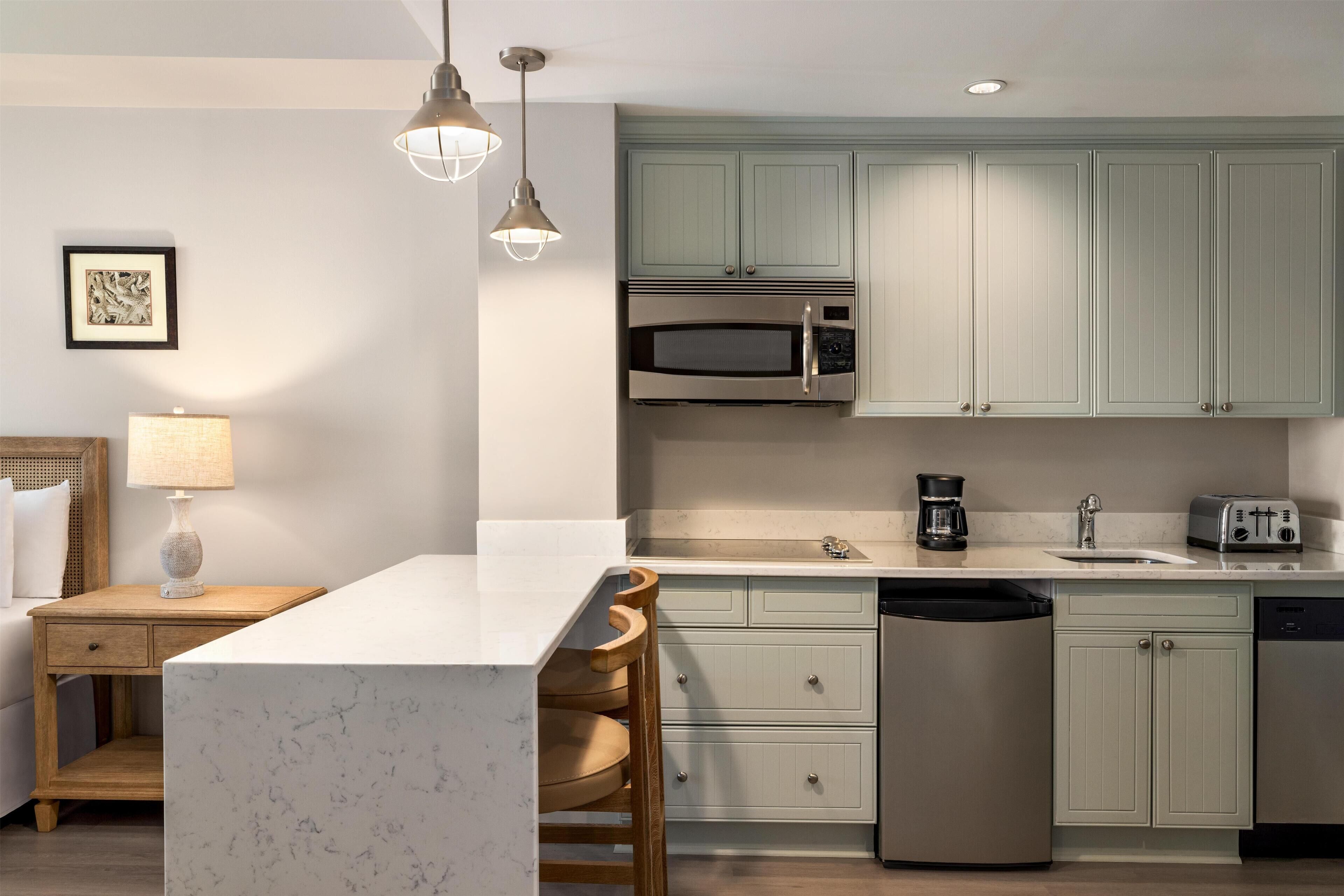 A modern kitchen with a marble island, built-in appliances, and light green cabinetry.