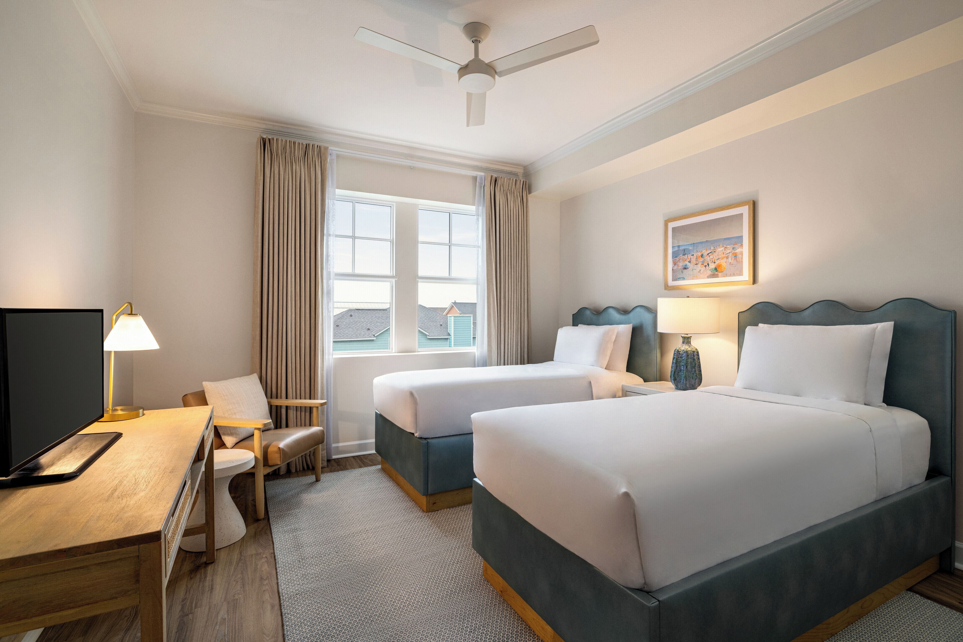 Une chambre d’hôtel avec deux lits, un bureau, une chaise, une télévision et un ventilateur de plafond.