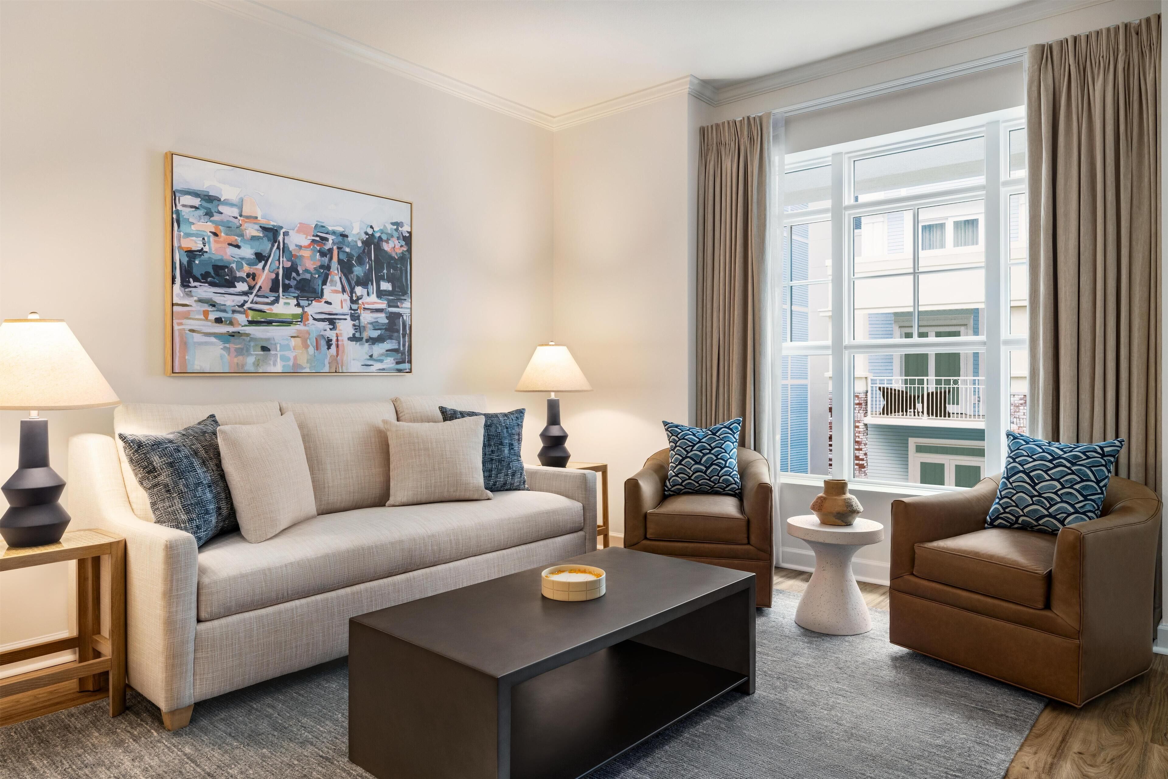 A modern living room with a sofa, two armchairs, a coffee table, and a painting on the wall.