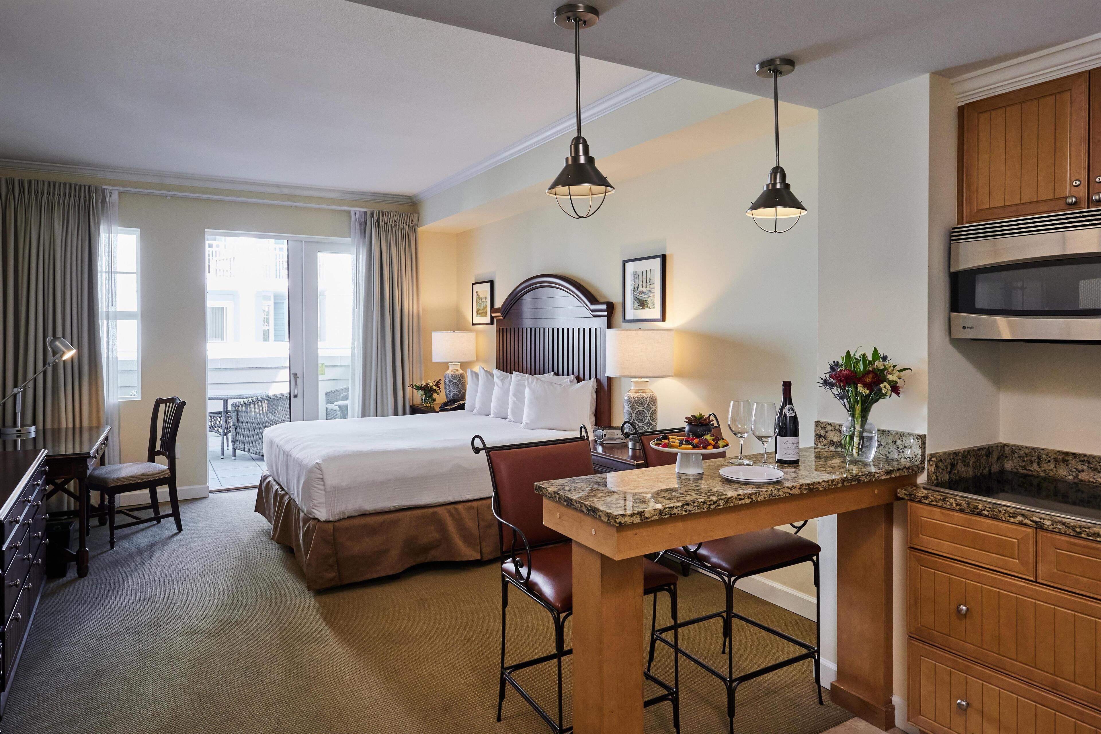 A hotel room with a bed, a desk, a kitchenette, and a view of the city.