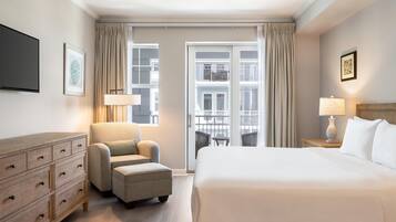 Habitación de hotel con una cama grande, un sofá, un aparador de madera, un televisor y un balcón con vistas a edificios.