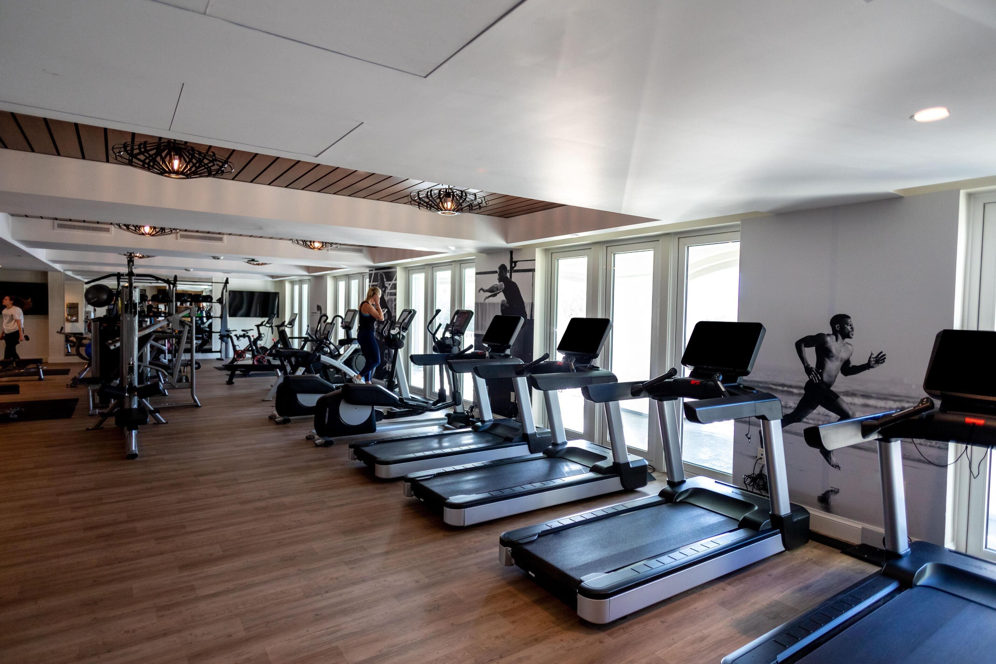 Une salle de sport équipée de plusieurs tapis de course, de vélos d’exercice et d’appareils de musculation.
