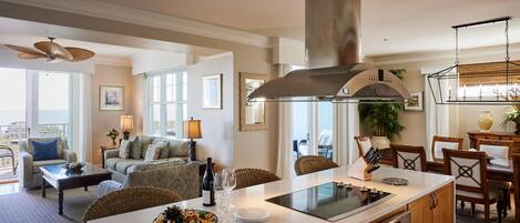A spacious living room with a large window, a dining area with a table and chairs, and a kitchen with a central island.