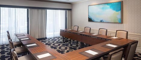 A conference room with a long table, chairs, a chandelier, and a large abstract painting on the wall.