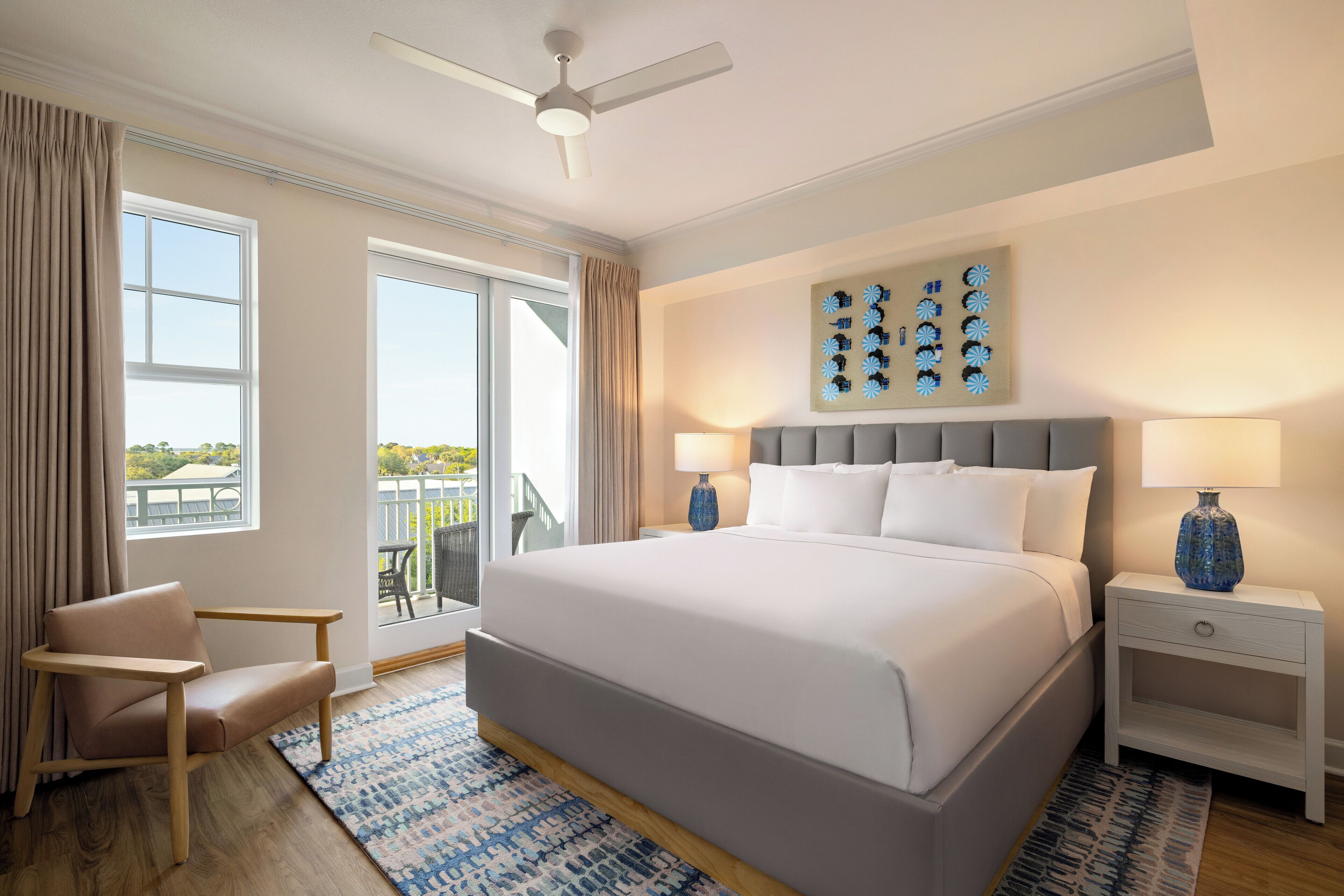 A hotel room with a large bed, two bedside tables, a ceiling fan, and a view of the outdoors.