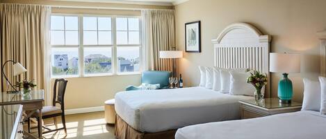 A hotel room with two beds, a desk with a chair, a lamp, and a view of the outside.