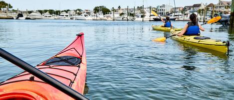 A marina with kayaks and boats, calm water, and houses in the background.