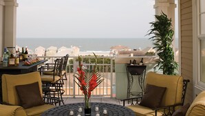 Ein Balkon mit Meerblick, ausgestattet mit gelben Stühlen und einem Tisch, und geschmückt mit Blumen und Kerzen.