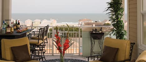 Un balcon donnant sur l’océan, agrémenté de chaises jaunes et d’une table, et décoré de fleurs et de bougies.