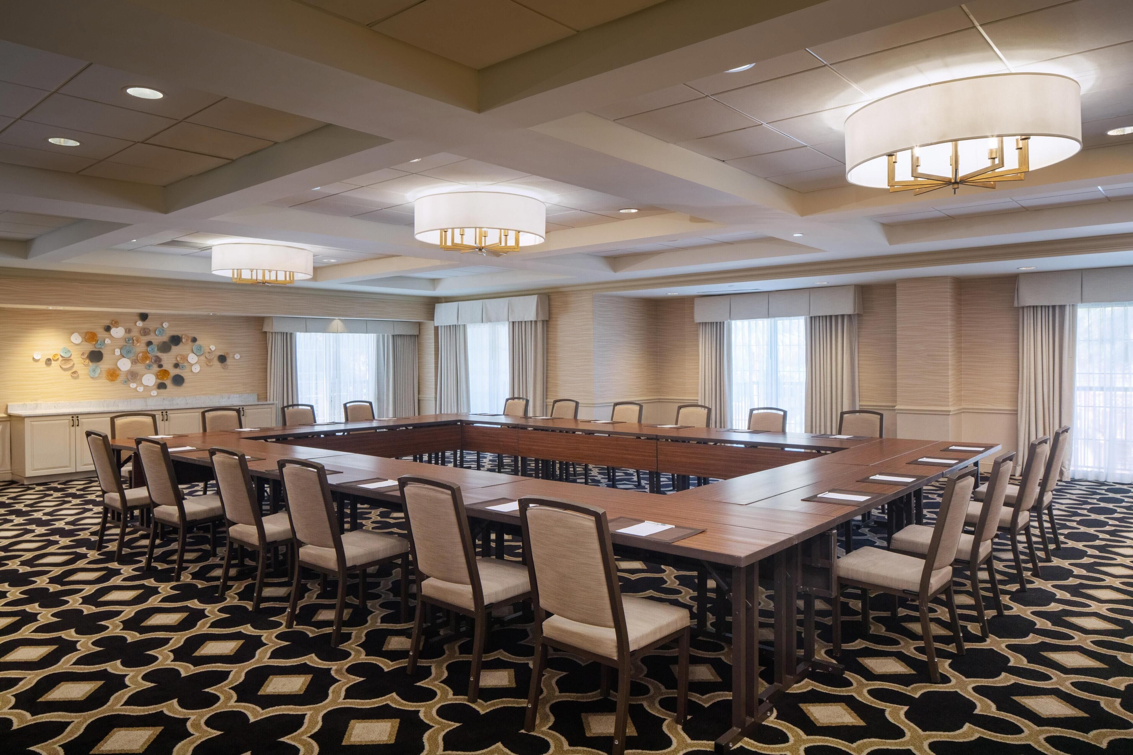 A conference room with a large rectangular table surrounded by chairs, a patterned carpet, and a chandelier.