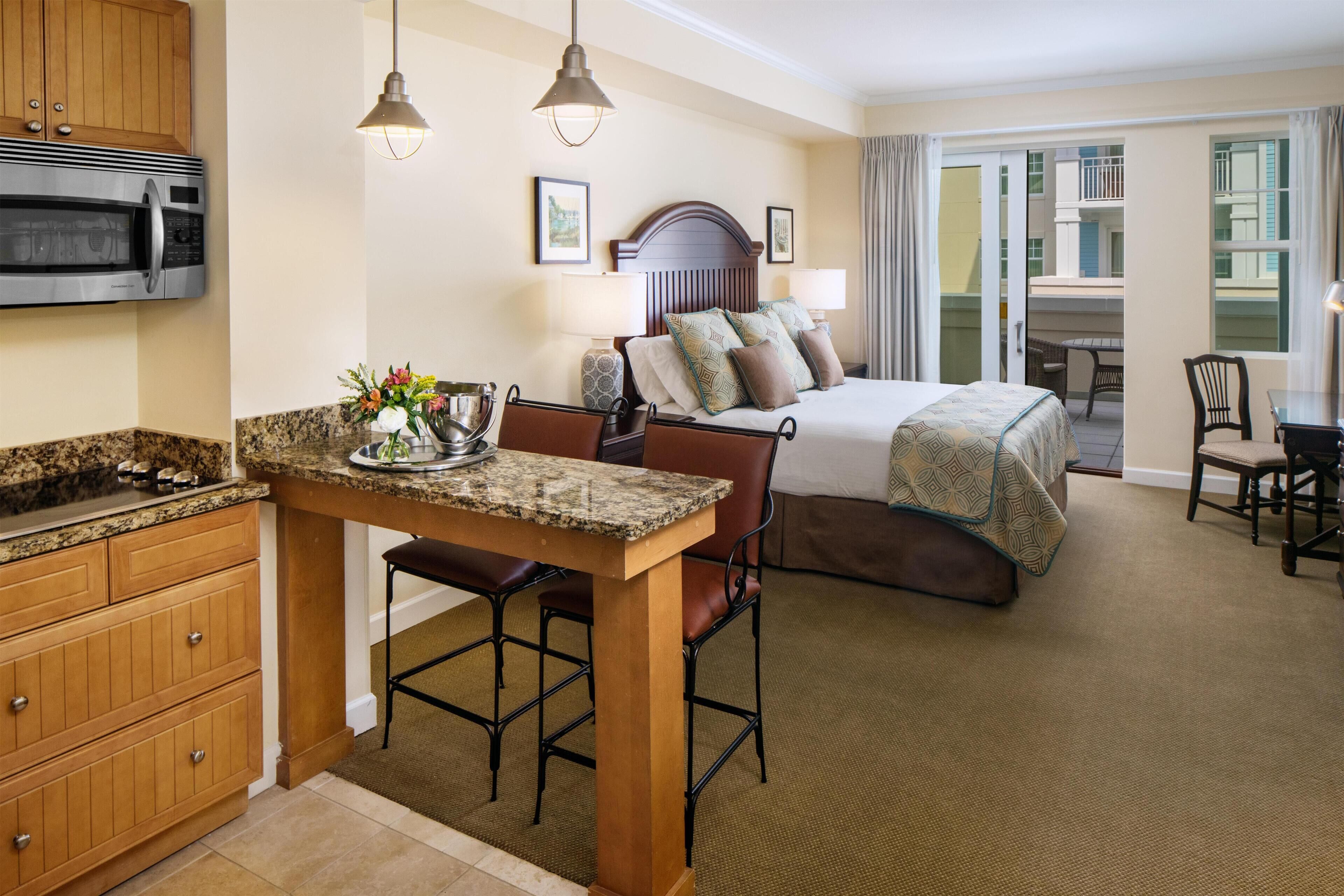 Une chambre d’hôtel avec un coin cuisine, une table à manger, un lit avec une tête de lit et un balcon avec vue.