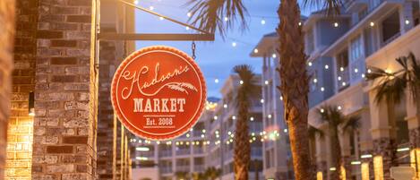 A street view with a sign for Hudson's Market, palm trees, and string lights.