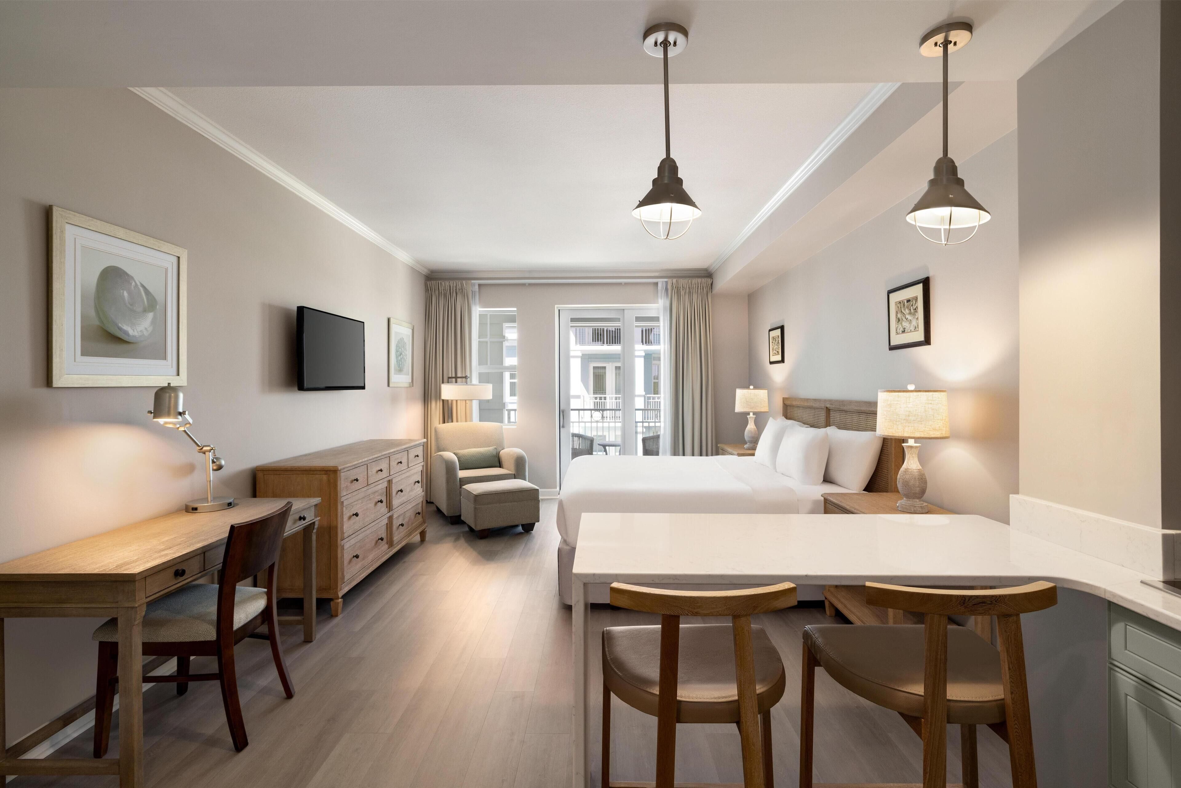 A hotel room with a bed, desk, chairs, and a TV.