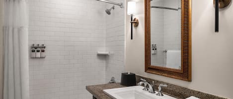 Un baño moderno con ducha, lavamanos, espejo y artículos de aseo.