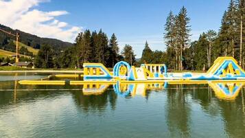 Un parc aquatique doté de structures de jeux gonflables et d’un lac paisible, entouré d’arbres et de collines.