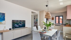 Moderni keittiö, jossa on ruokailutila. Keittiössä on suuri televisio, valkoiset kaapit ja ruokapöytä neljälle henkilölle.