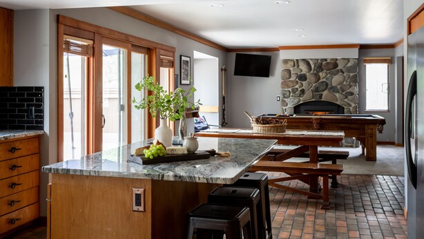 A spacious kitchen with a large island, wooden cabinets, and a stone fireplace. - Skylight by AvantStay | Elevated Mountain Home w/ Hot Tub, Billiards,Large Patio (Sunriver)