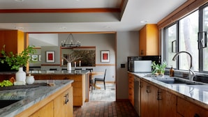 A modern kitchen with wooden cabinets, a marble countertop, and a large window. - Skylight by AvantStay | Elevated Mountain Home w/ Hot Tub, Billiards,Large Patio (Sunriver)