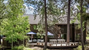 A wooden cabin with a deck, outdoor seating, and a covered area with umbrellas. - Skylight by AvantStay | Elevated Mountain Home w/ Hot Tub, Billiards,Large Patio (Sunriver)