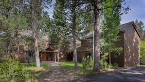 A rustic cabin with a brick pathway leading to the entrance, surrounded by tall pine trees. - Skylight by AvantStay | Elevated Mountain Home w/ Hot Tub, Billiards,Large Patio (Sunriver)