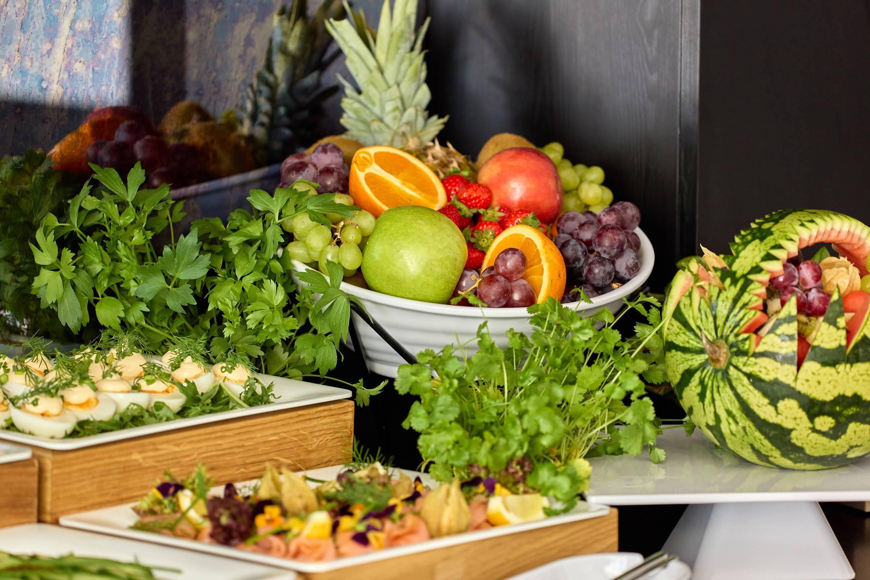 Ein reichhaltiges Buffet mit verschiedenen Speisen, darunter Obst, Gemüse und eine Wassermelone.