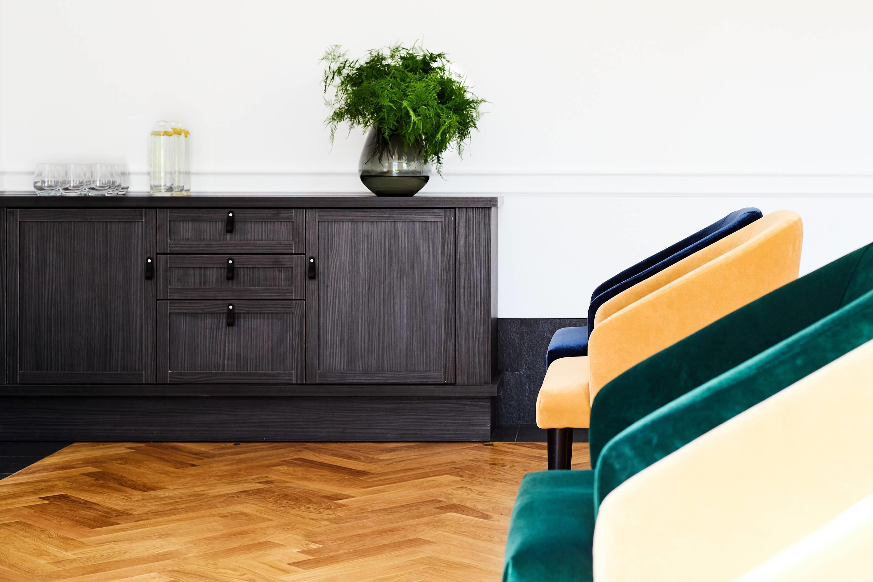 A room with a dark wooden cabinet, a potted plant, and a chair with a cushion.