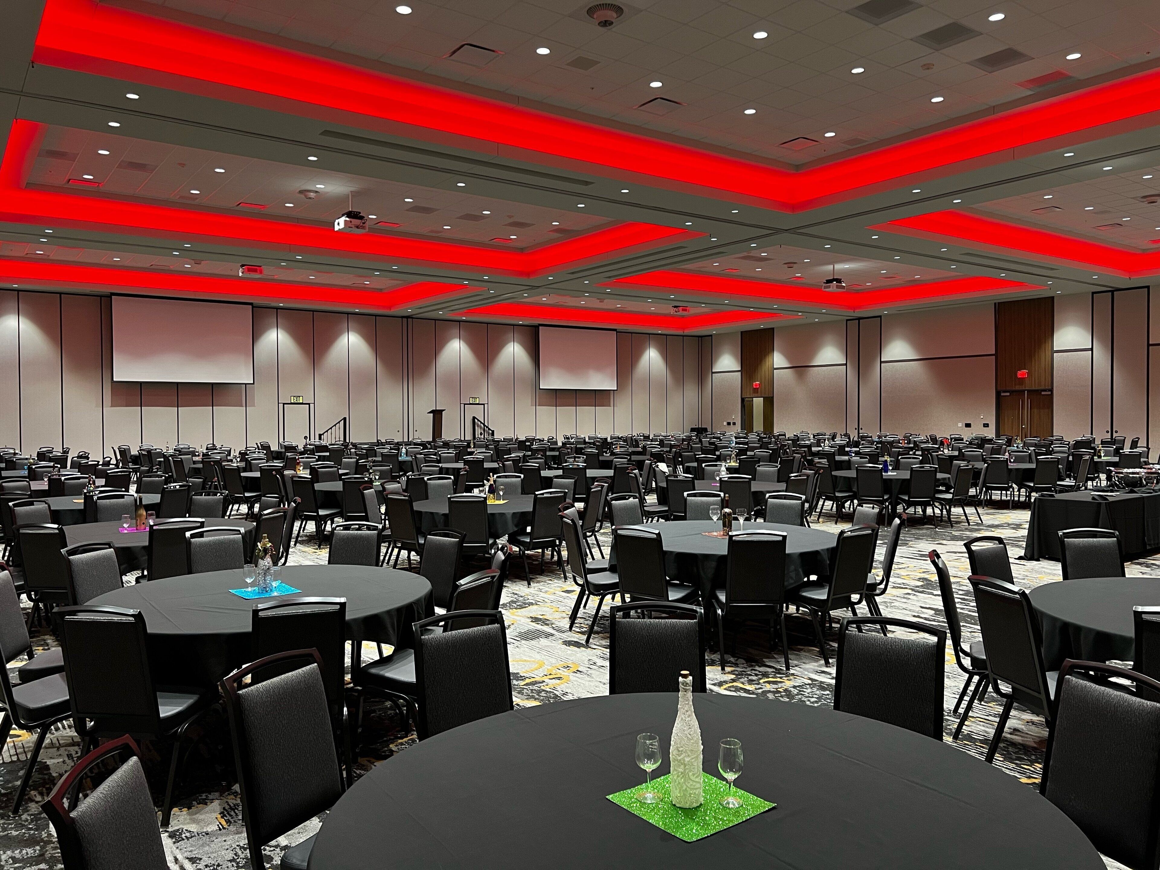 A large conference room with multiple tables and chairs, equipped with projectors and screens on the walls.