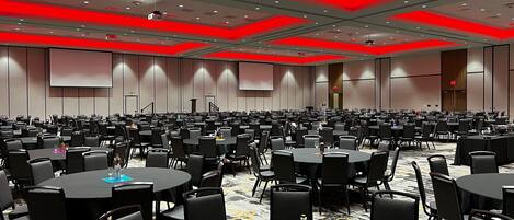 A large conference room with multiple tables and chairs, equipped with projectors and screens on the walls.