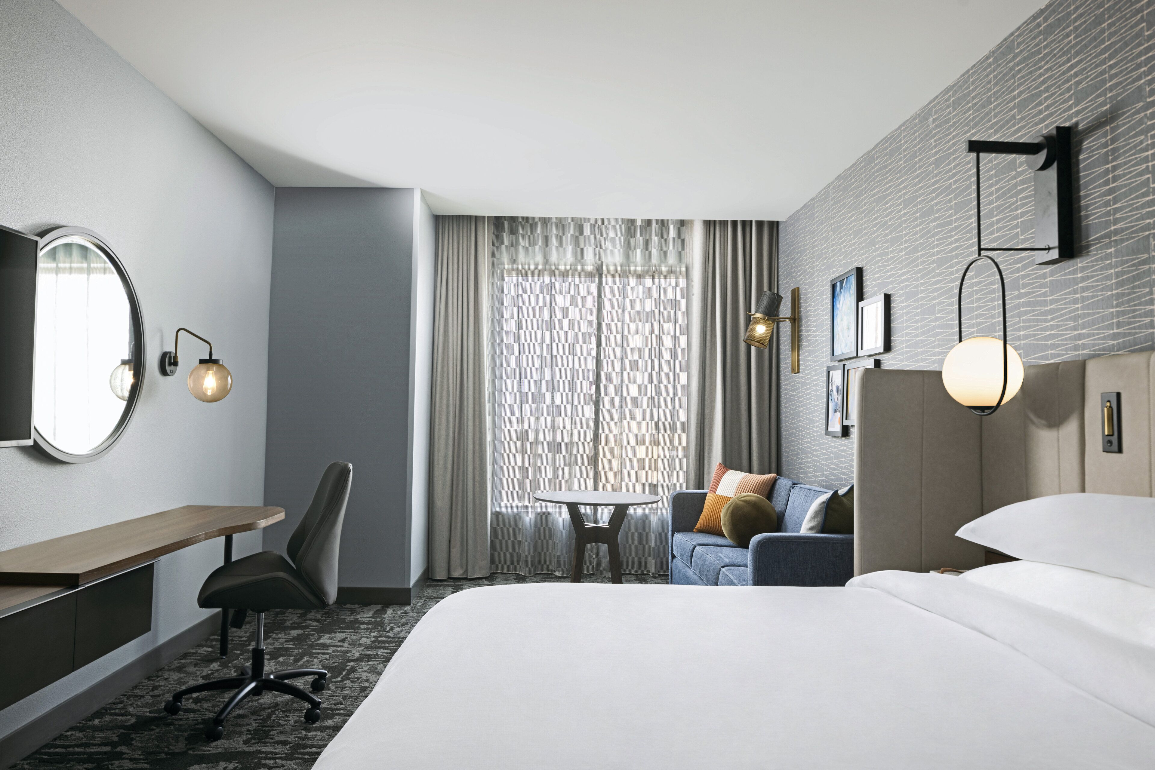 A hotel room with a bed, a desk, a chair, a small table, and a sofa.