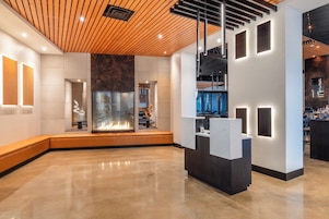 Un vestíbulo moderno con techo de madera, una chimenea central y un mostrador de recepción con paneles iluminados.