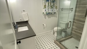 Un baño con cabina de ducha de vidrio, un inodoro y un lavamanos con una toalla colgada en la pared.