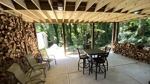 Un patio al aire libre con una mesa y sillas, rodeado de leña apilada y un muro de piedra.