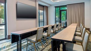 A conference room with a long table, chairs, a flat-screen TV, and large windows with curtains.