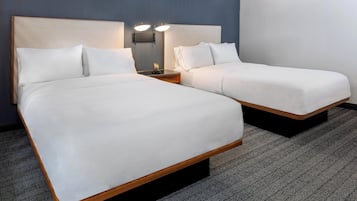 Habitación de hotel con dos camas individuales, una mesita de noche con lámpara y suelo cubierto de alfombra.