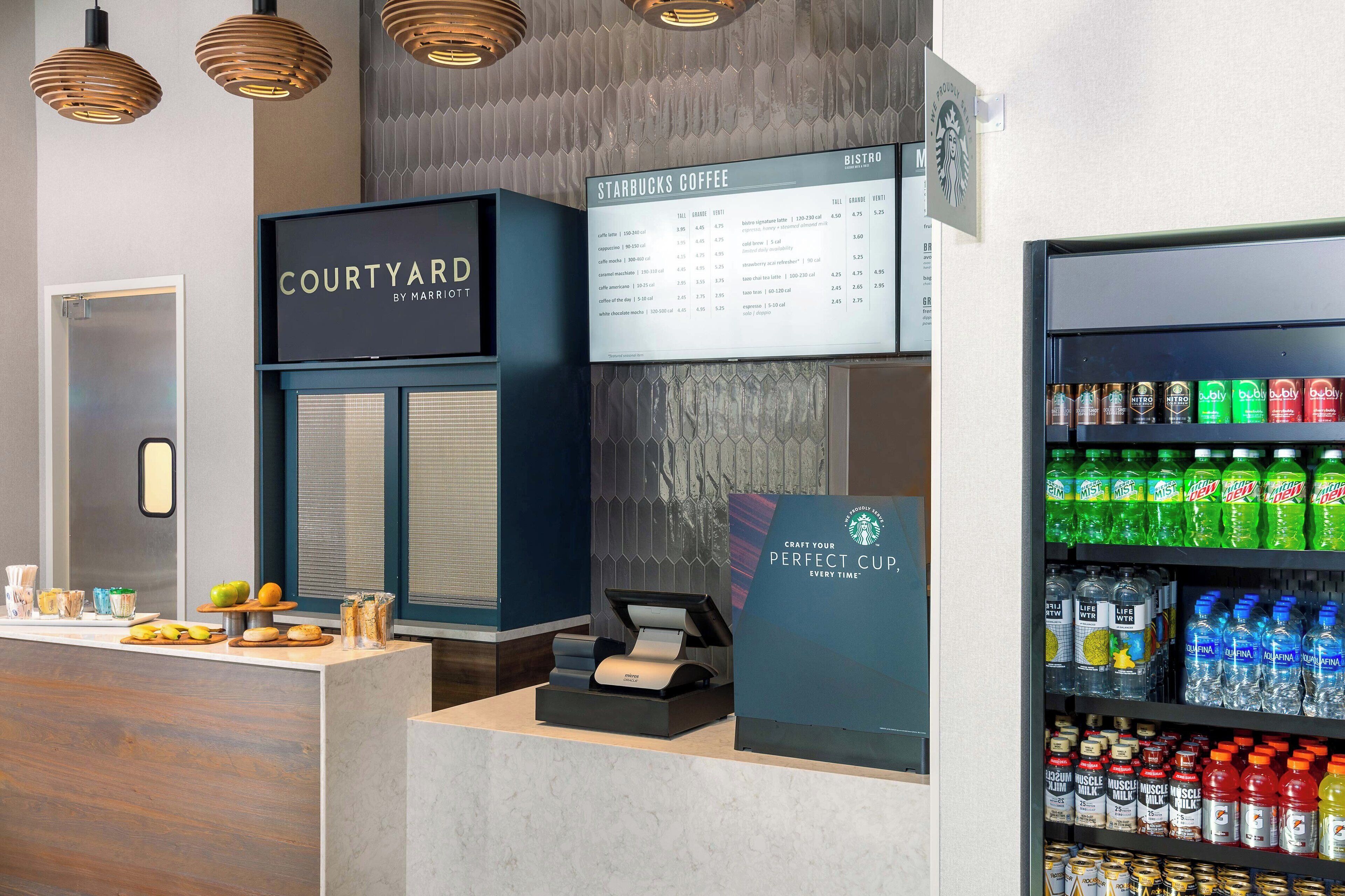 A Starbucks Coffee station with a menu board, a refrigerated drink display, and a counter with pastries and a coffee machine.