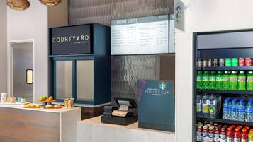 A Starbucks Coffee station with a menu board, a refrigerated drink display, and a counter with pastries and a coffee machine.