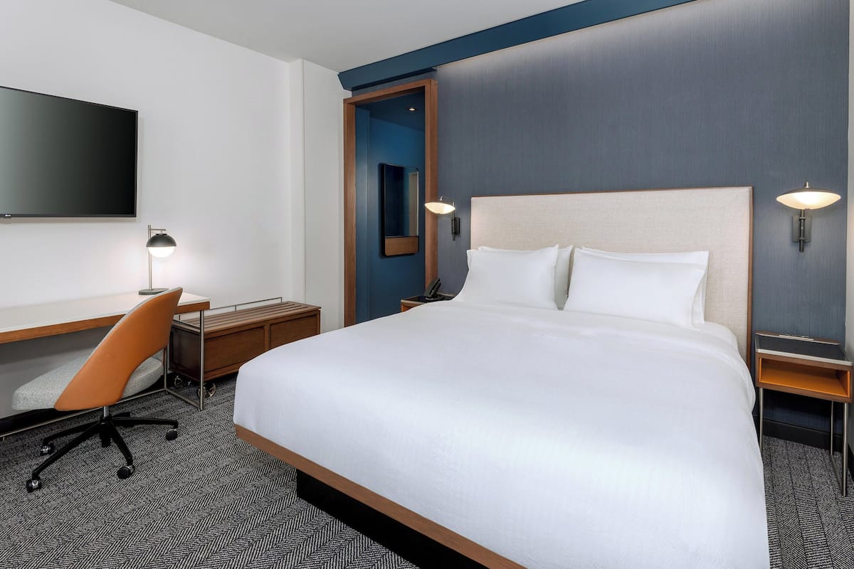 A hotel room with a large bed, a desk with a chair, a flat-screen TV, and two wall-mounted lamps.