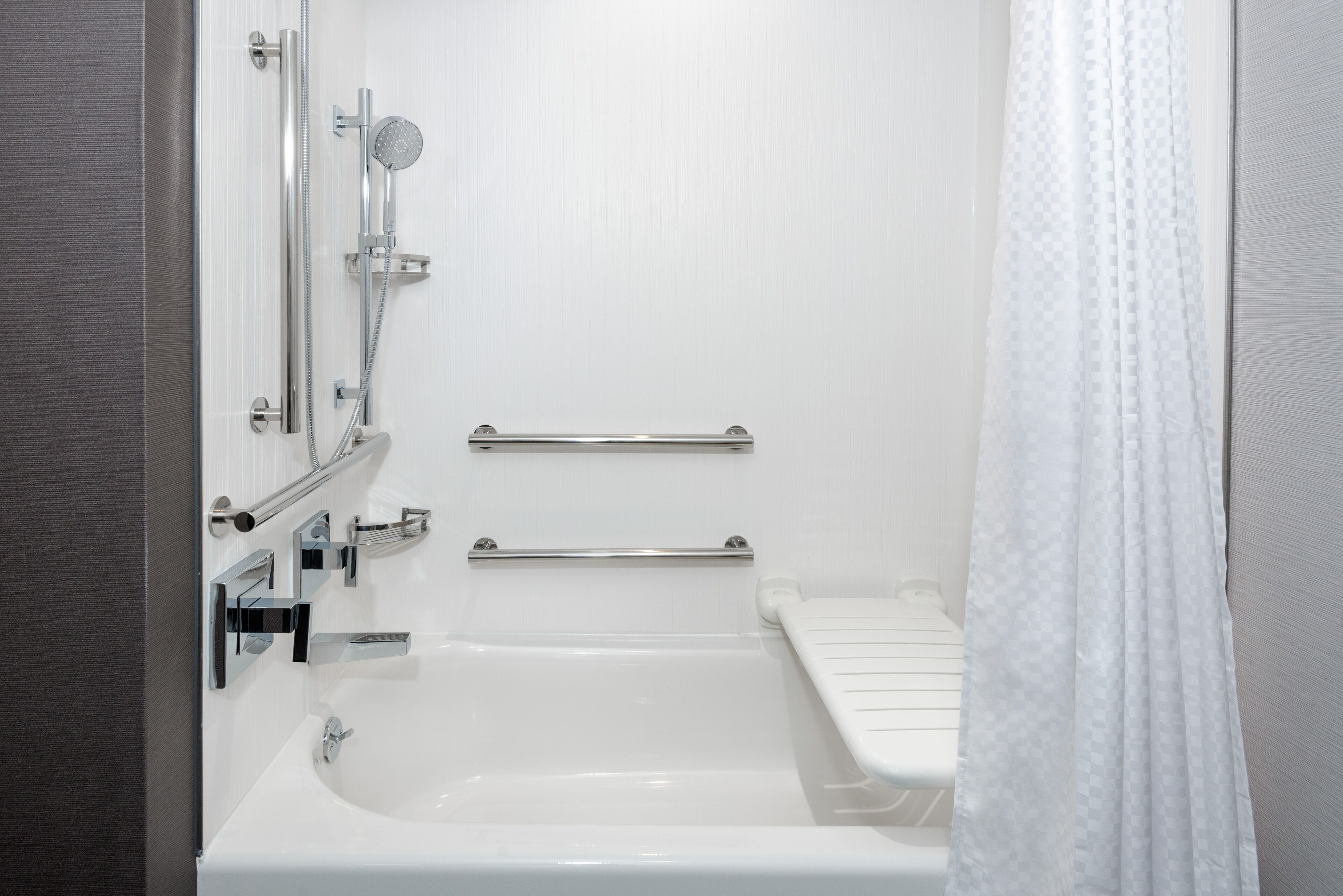 A modern bathroom with a bathtub, shower, and handrails.