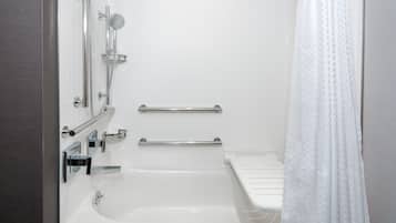 A modern bathroom with a bathtub, shower, and handrails.
