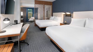 A hotel room with two beds, a desk, a chair, a TV, and a view of the city. - Courtyard by Marriott Atlanta Midtown (Atlanta)