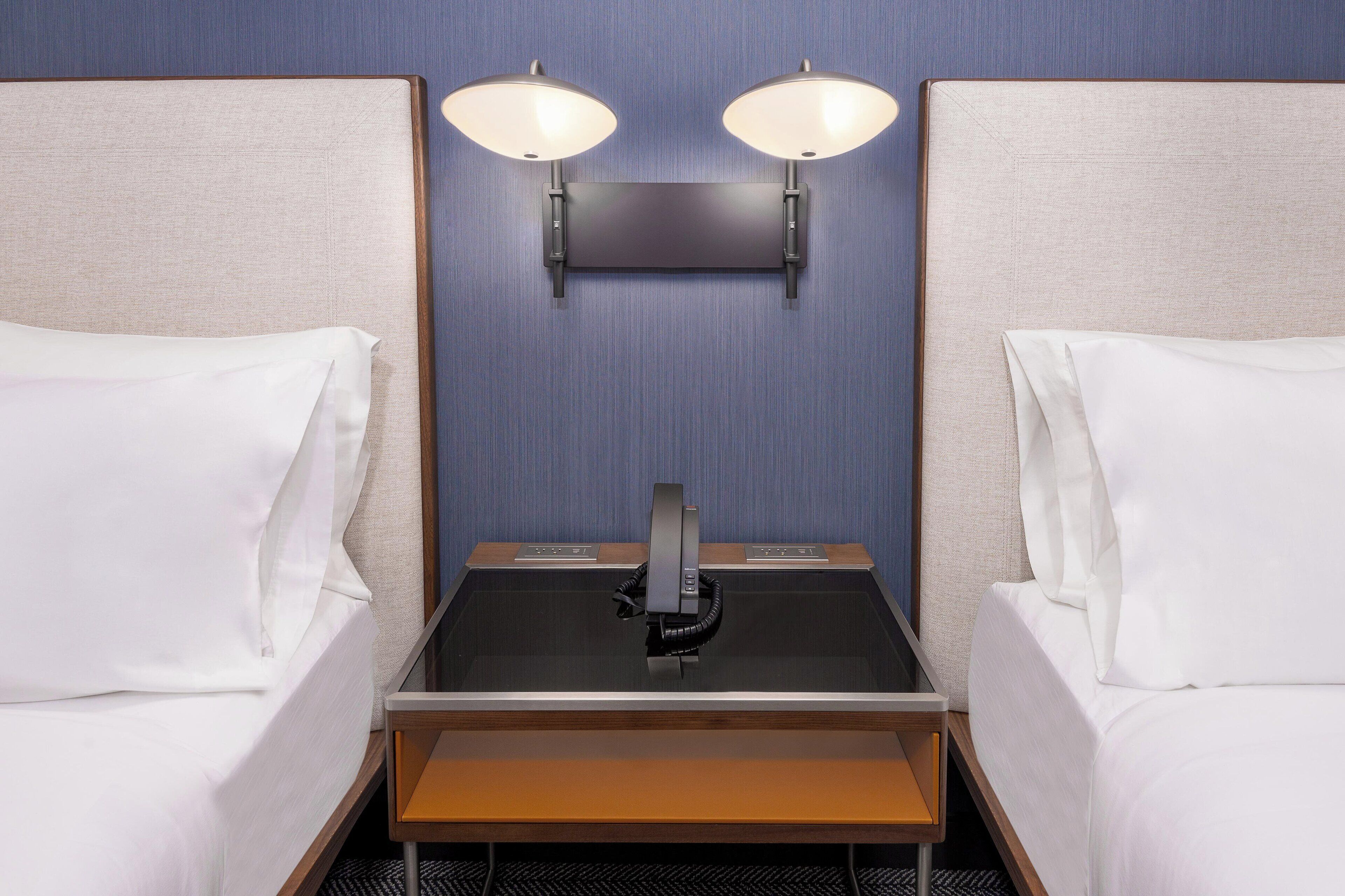 Habitació d'hotel amb dos llits, una taula de nit, televisió de pantalla plana i làmpades penjades a la paret.