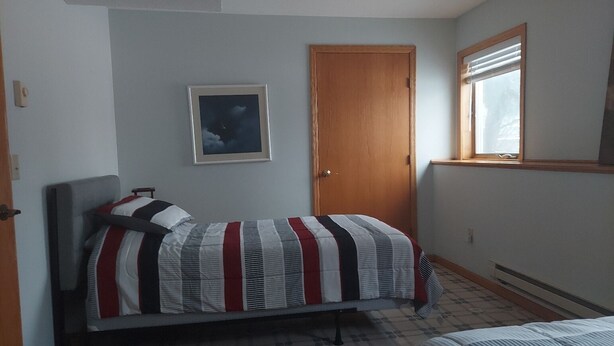 A bedroom with a bed, a door, a window, and a framed picture on the wall.