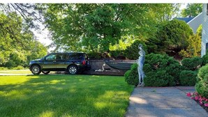 A driveway with a parked SUV, a statue, and well-maintained landscaping.